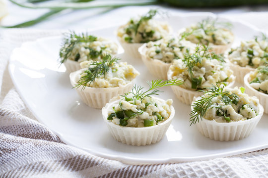 Tartlets with cheese and green onion filling decorated with dill on a dish