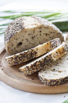 Sliced homemade bread loaf with sesame and other grains on a round desk at wooden table