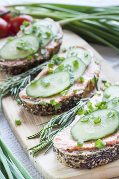 Sandwiches with fish butter, cucumber and herbs on wooden board for a snack breakfast