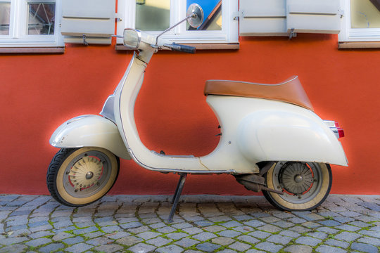 Alter weißer Motorroller parkt vor roter Hauswand