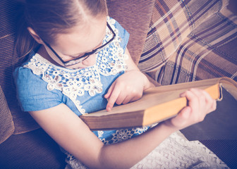Girl reading a book at home sitting in an armchair.
