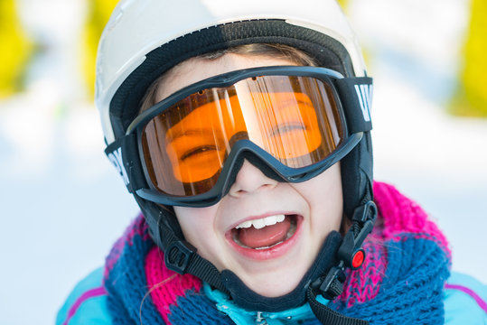 Ski, skier girl, winter vacation - happy child girl in goggles and protective helmet enjoining winter holidays