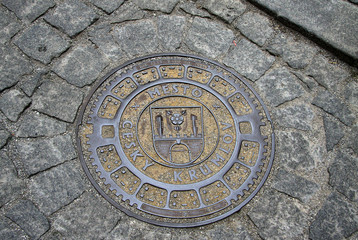 Fototapeta na wymiar CESKY KRUMLOV, CZECH REPUBLIC - MAY 01, 2013: Round steel sewer manhole on old cobblestone road in Cesky Krumlov, Czech Republic