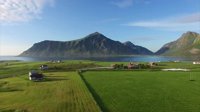 Aerial footage of green fields contrasting with red houses and church in scenic village Flakstad on Lofoten islands in Norway. Aerial 4k Ultra HD.