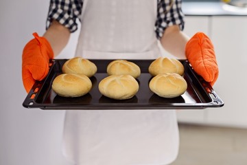 woman holding a baking tray with freshly baked bread rolls.