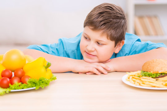 Chubby kid is looking at healthy food plate. 