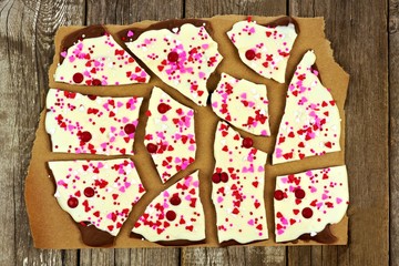 White and dark chocolate bark with candy heart sprinkles on paper against rustic wood