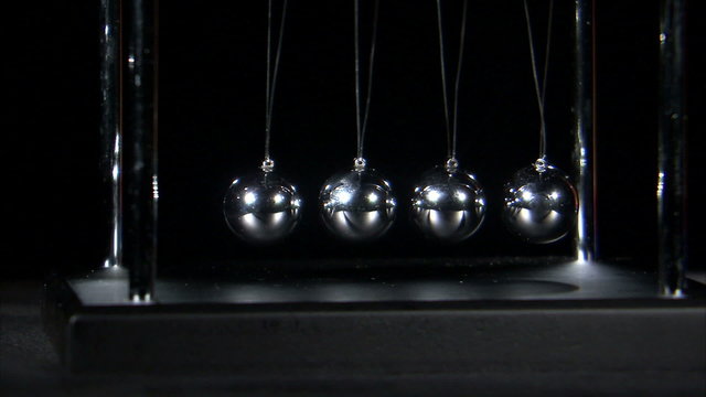 Newton's Cradle balls colliding on black background.