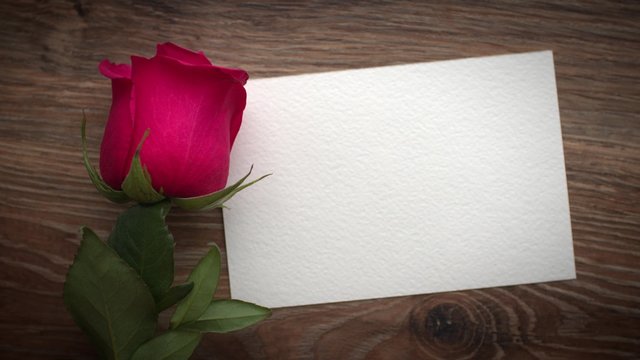 Man's hand puts a greeting card with a rose on the table. St. Valentine's Day