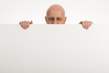 Bald man peeps over top of blank white paper