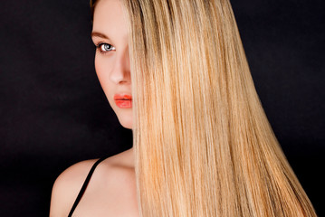 Beautiful young blonde woman with long straight hair on a dark background