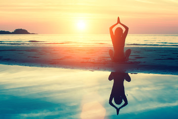 Silhouette meditation girl on the background of the stunning sea and sunset. Yoga, fitness and healthy lifestyle. Woman doing meditation near the ocean.