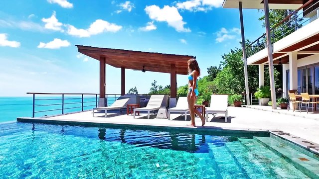 Outdoor lifestyle portrait of young pretty sexy girl posing with neon bright swimming mattress at the pool, wearing bikini and sunglasses, view on ocean, relax and having fun on vacation.