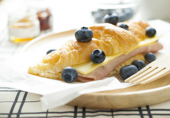 Fresh croissants ham cheeze and blue berries on wooden plate