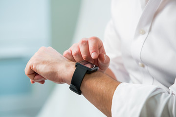 Man in white shirt using his smart watch. Close-up hands on interior background