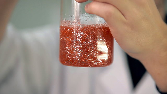 The laboratorian is mixing the ingredients in a glass.