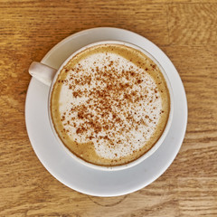 Cappuccino in white cup close-up on wood background