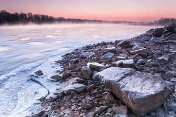 Stony bank of a freezing river covered in fog during dusk