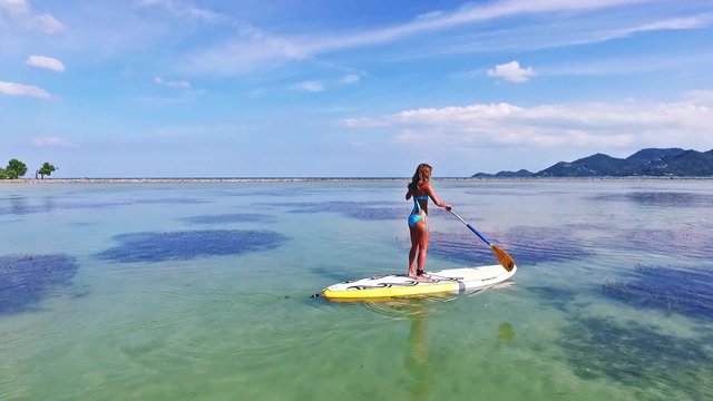 Stand up paddle board woman paddleboarding on SUP on Samui Thailand standing happy on paddleboard on in water. Young female model on Thailand beach on summer holidays vacation