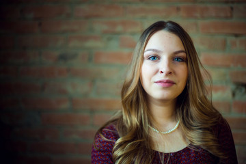 Fototapeta premium A young female fashion model in dress against a brick wall background. She is looking at.