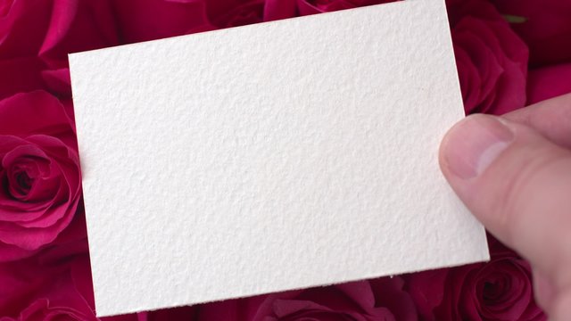 Man's hand puts a greeting card with a rose on the table. St. Valentine's Day