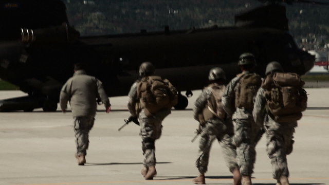 Soldiers walking towards a waiting CH-47 Chinook Helicopter at an airfield.