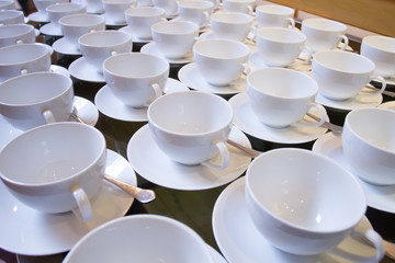 Stacked empty teacups with teaspoons at a function over white ba