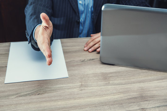 datore di lavoro seduto alla scrivania con contratto e notebook che stringe la mano 