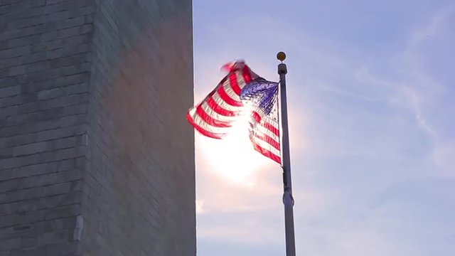 A static shot with a lens flare of an american flag to the side of the Washington Monument.