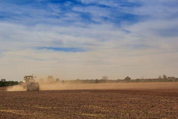 blue sky fleecy clouds above field tractor in great dust cloud