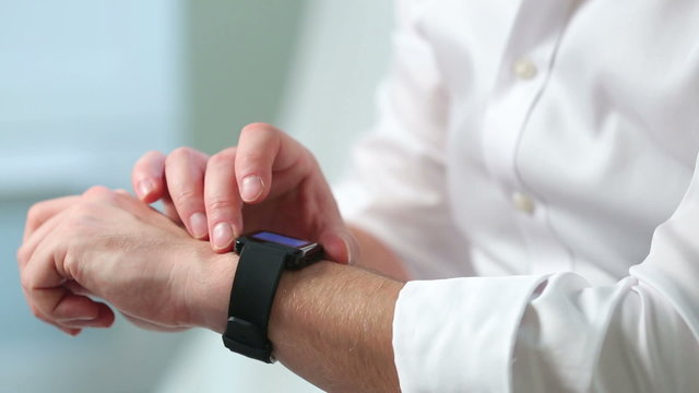 A man in a white shirt uses a smart watch. Close-up.