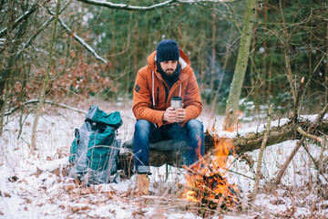hiker warming hands at campfire in winter forest