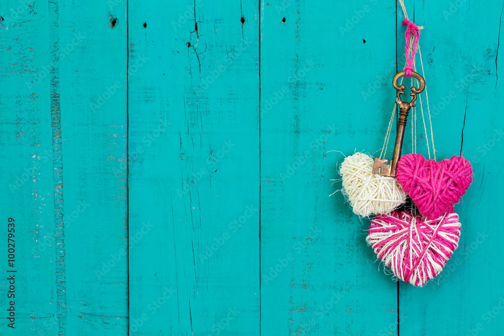 Wall mural Skeleton key and pink hearts hanging on teal blue wood background