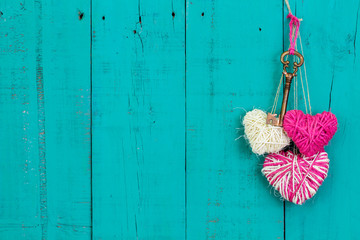 Skeleton key and pink hearts hanging on teal blue wood background