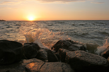 The wave hits the shore rocks lit by the setting sun. Transparen
