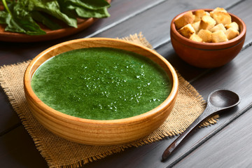 Fresh homemade cream of spinach soup in wooden bowl, photographed on dark wood with natural light...