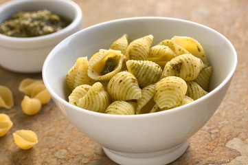 Pesto alla genovese on shell pasta. Pesto is a traditional basil sauce for pasta in the Italian cuisine. Photographed on slate with natural light (Selective Focus, Focus in the middle of the pasta)