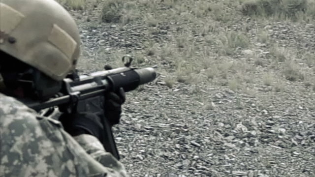 Static shot, soldier shooting automatic small target rifle at range while kneeling.