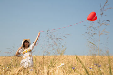 Romantisches junges Mädchen im Weizen Feld mit Herz Ballon in Rot.  Konzept Hintergrund für...