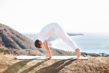 Asian man meditates in yoga position on high mountains above blue sky. 