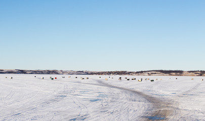 Groups of multiple ice fishing shacks on a snow covered lake in a winter landscape