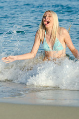 Blonde woman with amazing slim body wear bikini kneeling in the sea, waves hitting her body