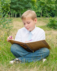 Schoolboy sitting in the park and writing in a notebook