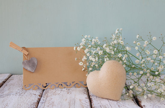 fresh white flowers, heart next to vintage empty card over wooden table.