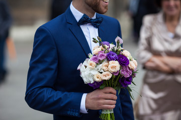 Handsome confident groom in blue suit holding purple wedding bouquet closeup