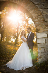 Fairytale romantic valentyne newlywed couple hugging and posing under old castle bridge at sunset in autumn