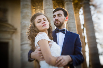 Obraz premium Sensual romantic newlywed bride and groom hugging in front of old baroque church with columns at sunset closeup