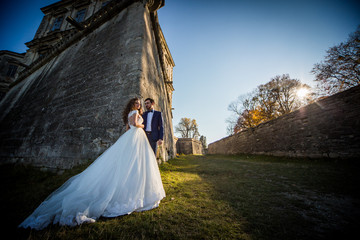 Romantic fairytale couple of newlyweds posing at sunset near old baroque castle wall