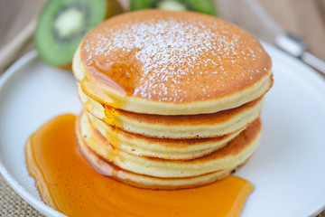 pour syrup on stack of pancake on white plate and sackcloth with