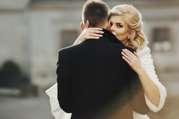Beautiful blonde bride kissing handsome groom in black coat in t